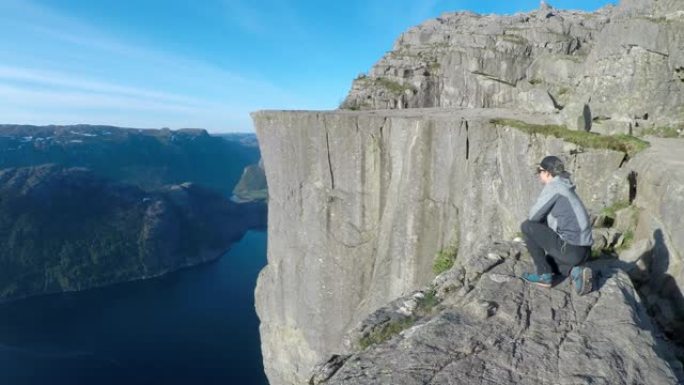 一名男子走在挪威Preikestolen附近的悬崖边缘。他正俯伏在深渊之上。危险的位置。在他身后的L