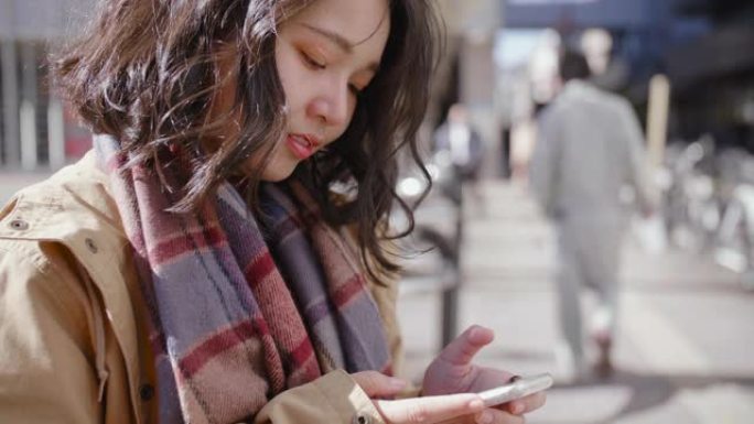 年轻女子发短信，在智能手机上思考和回复。在繁忙的地区微笑。