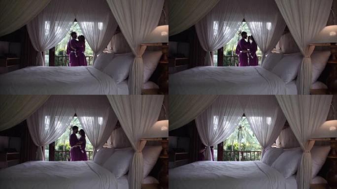 新婚夫妇穿着浴袍拥抱在一个豪华的酒店，有一张大顶篷床。