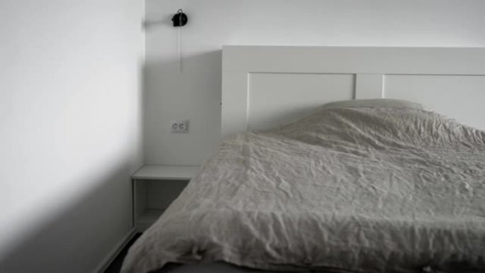 现代卧室的内部。明亮的房间，白色墙壁，宽大的床，毯子和枕头