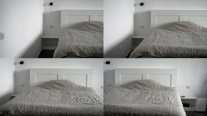 现代卧室的内部。明亮的房间，白色墙壁，宽大的床，毯子和枕头