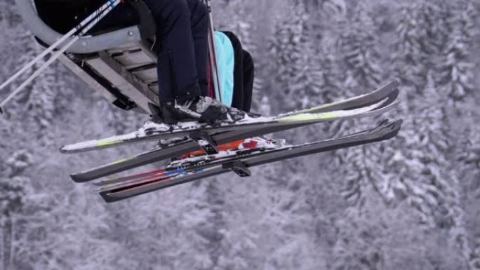 滑雪缆车上的滑雪者。在森林中白雪皑皑的松树的背景下，用滑雪板和滑雪靴的腿