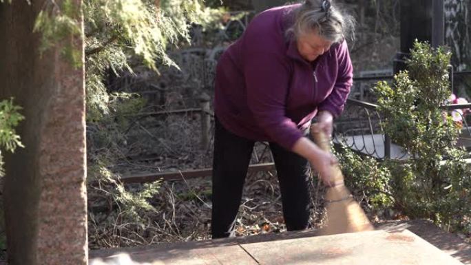 参观墓地的老年妇女。女人清理花岗岩墓碑上的碎片。