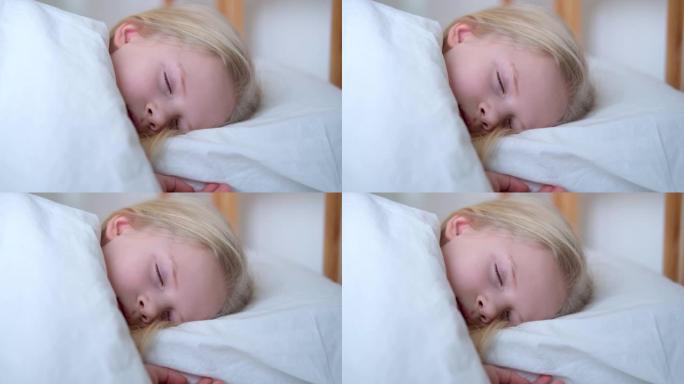 睡觉的金发小女孩一大早就在大床上用白色床上用品特写镜头。孩子们做梦。童年，平静，夜晚。4k镜头