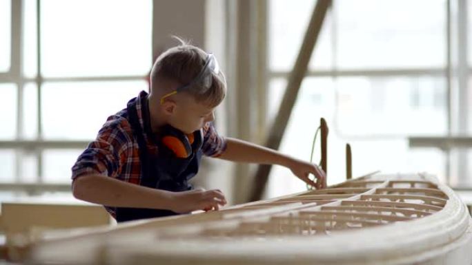 木工车间熟练男孩建造大型木制船模的侧视图