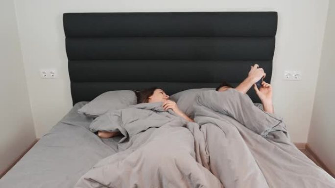 男女夫妇躺在床上放松的时间流逝。白人年轻夫妇在家里的灰色床上