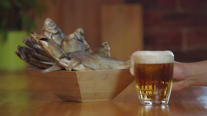 一杯冷新鲜啤酒放在木条上。小吃啤酒。带干鱼的木碗。