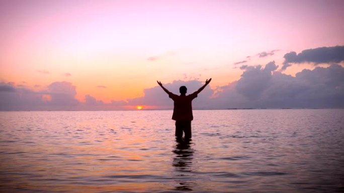 男子在平静的海洋中举起双臂做礼拜姿势，晨曦