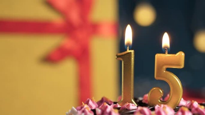 生日蛋糕15号点火器燃烧的金色蜡烛，蓝色背景礼物黄色盒子用红丝带绑起来。特写和慢动作