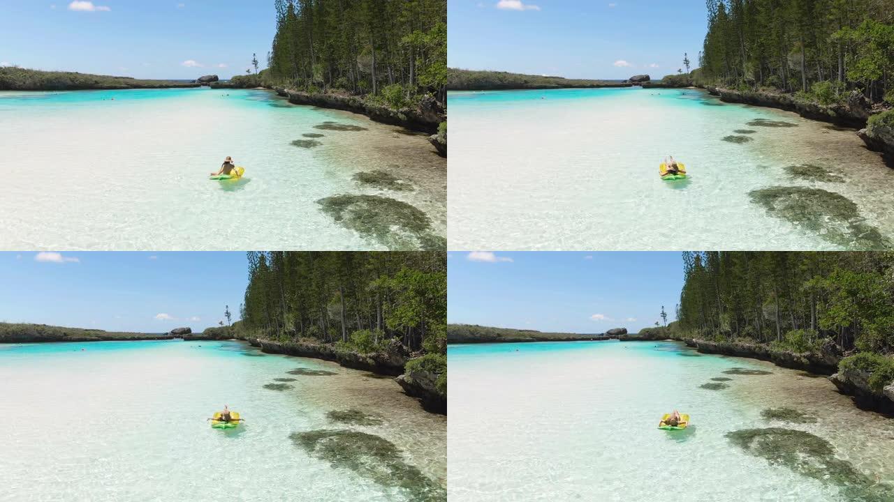 女孩在充气水果上的航拍画面，在新喀里多尼亚的松岛上的天然游泳池。游客在清澈的蓝色水中。太平洋旅游。