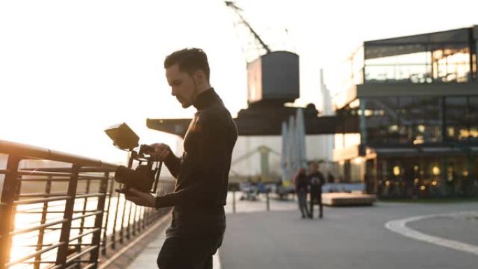 在大城市日落时手持电影制片人相机。人们在后台奔跑