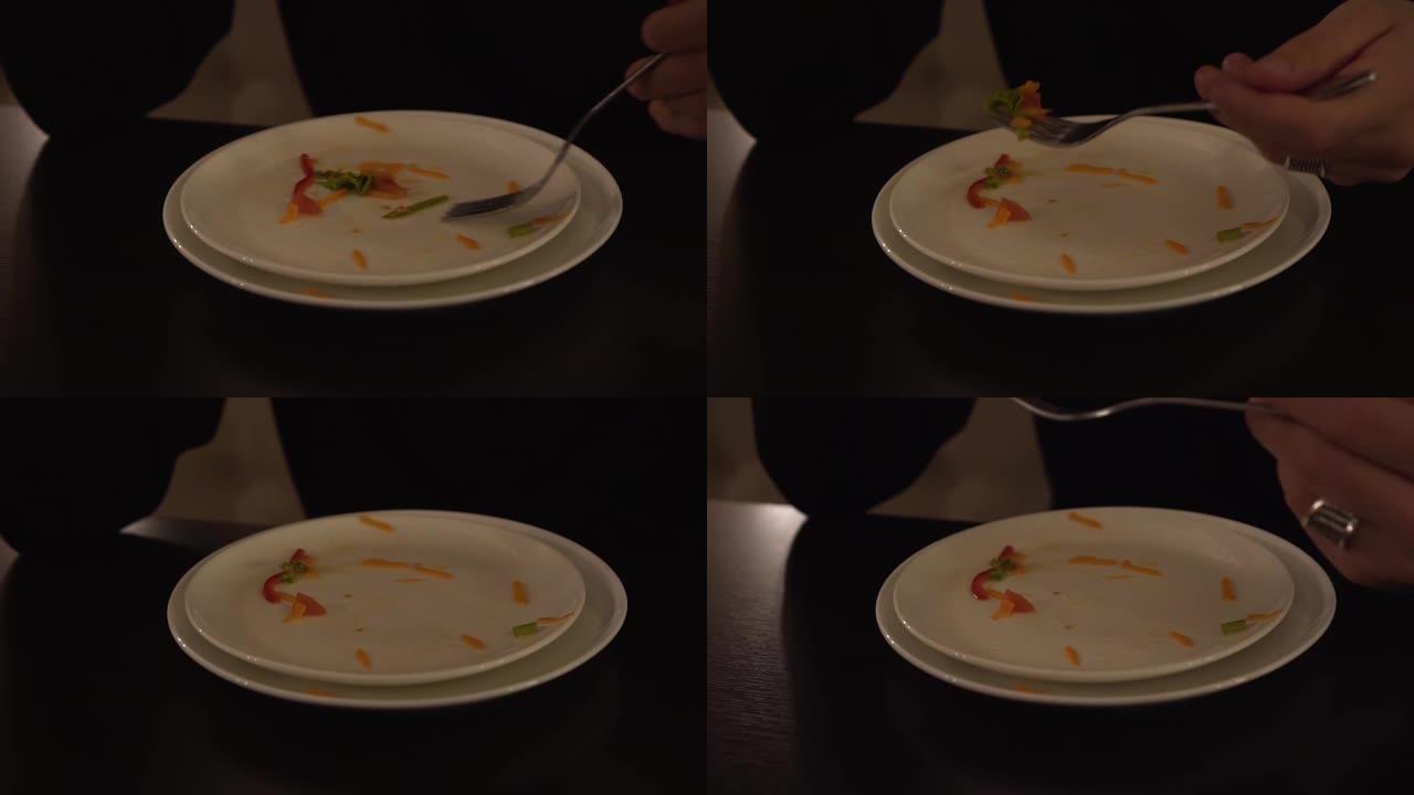 一只雄性手用叉子从白色盘子里收集剩余的食物。盘子里剩下的蔬菜沙拉很容易吃