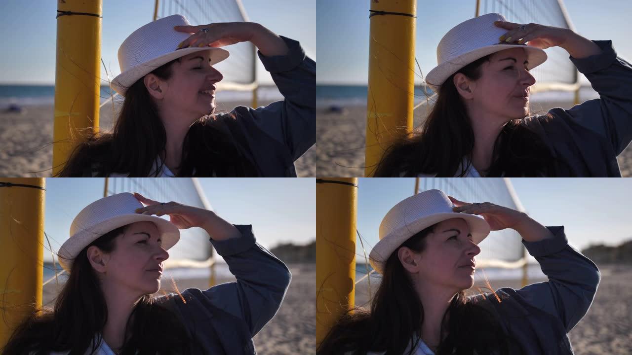 戴着帽子的幸福女人站在沙滩上环顾四周