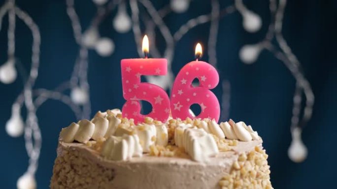 蓝色背景上有56号粉色蜡烛的生日蛋糕。蜡烛吹灭了。慢动作和特写视图