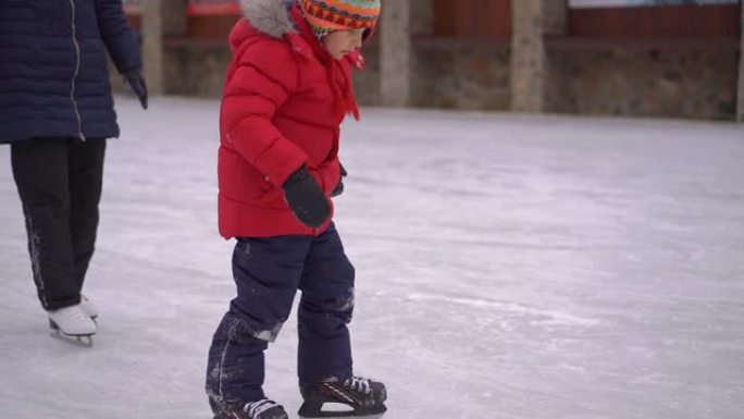 年轻的妈妈和一个小男孩在溜冰场上。小男孩学习如何滑冰。冬季活动概念