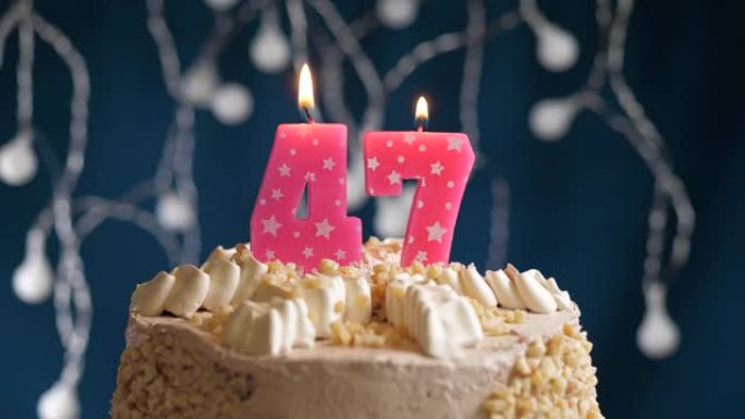 蓝色背景上有47号粉色蜡烛的生日蛋糕。蜡烛吹灭了。慢动作和特写视图