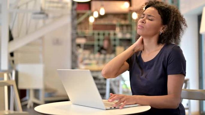 年轻的非洲妇女在咖啡馆使用笔记本电脑时颈部疼痛