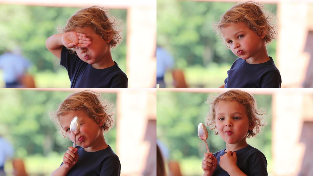 金发小男孩躲在镜头前，手和勺子可爱可爱