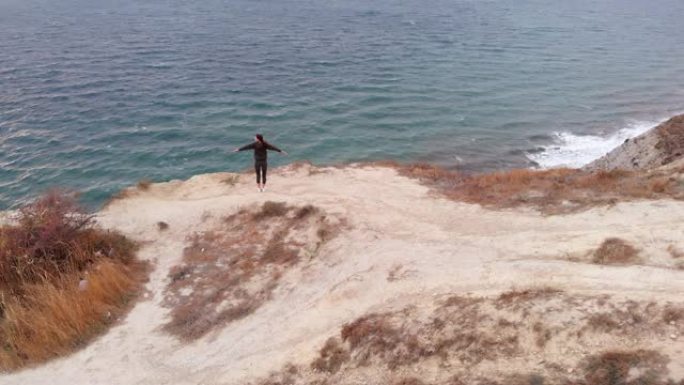 考虑到环境，一名年轻女子站在海洋上方的悬崖边缘练习瑜伽。体式、能量和冥想