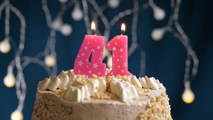 蓝色背景上有41号粉色蜡烛的生日蛋糕。蜡烛着火了。慢动作和特写视图
