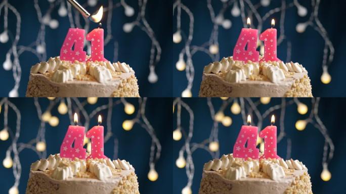 蓝色背景上有41号粉色蜡烛的生日蛋糕。蜡烛着火了。慢动作和特写视图