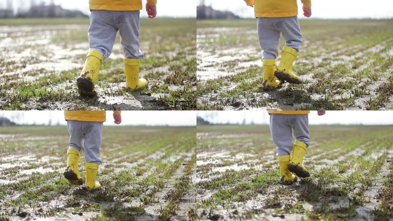 儿童腿穿着黄色泥泞的橡胶靴在湿泥上。