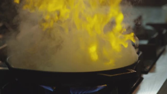 专业厨师烹饪flambe风格。在明火锅中准备盘子肉。厨师在商用厨房的煤气灶上油炸食物。男人在餐厅的滚