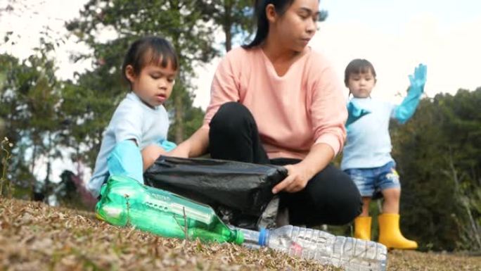 带着孩子在森林里收集垃圾的志愿者家庭。小女孩和戴着手套的母亲从公园的草地上捡起一个塑料瓶。保存环境和