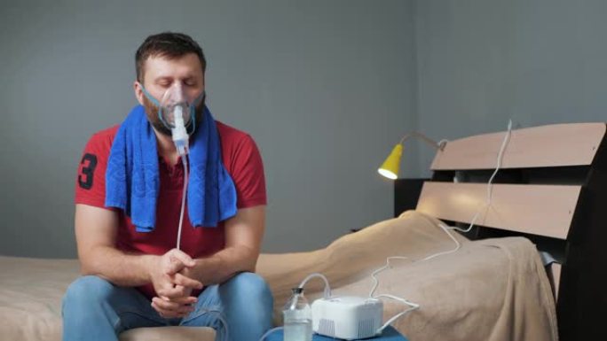 人类用喷雾器吸入。年轻人独自一人坐在房间里，戴着口罩在脸上吸气，呼吸着喷洒的盐水。慢动作和总体计划