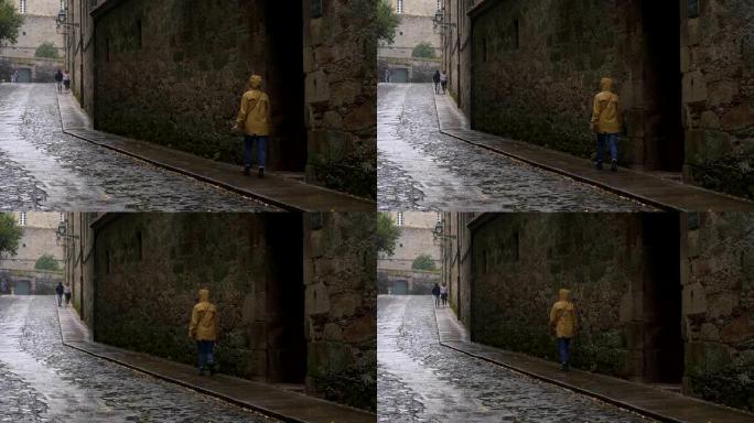 西班牙圣地亚哥德孔波斯特拉市，女旅行者穿着黄色夹克走在下雨天的街道上