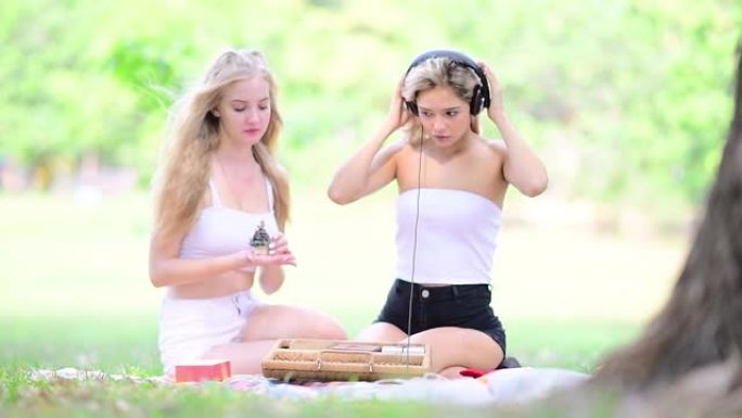 年轻的姐妹们一起在公园里用智能手机放松听音乐。