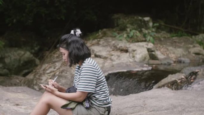 一个亚洲女孩坐在岩石上在笔记本上画素描。