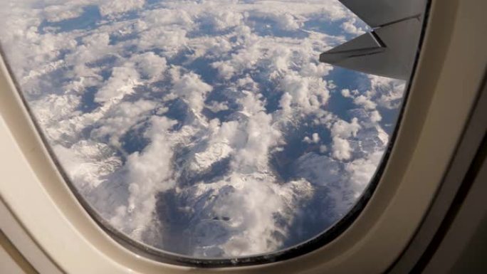 从飞机在雪地和云与冰川的山地断层上的窗户看
