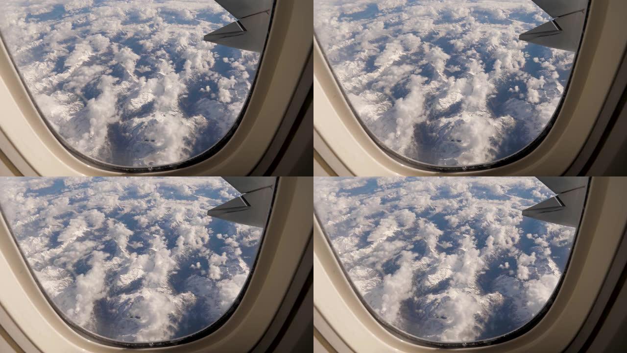 从飞机在雪地和云与冰川的山地断层上的窗户看