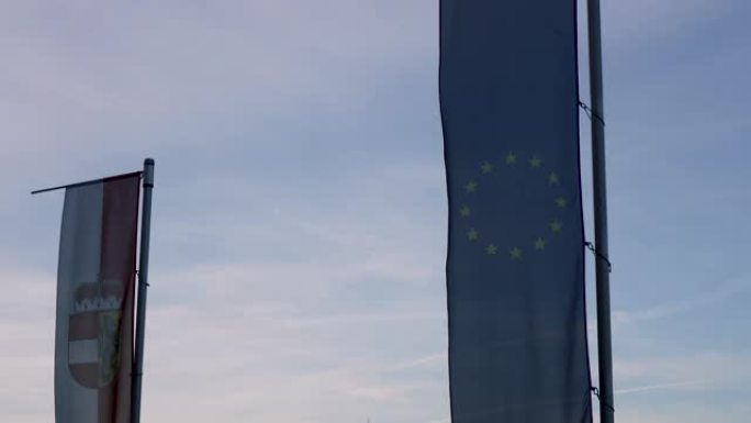 日落时旗杆上的欧盟国旗和萨尔茨堡州旗