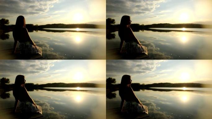 年轻女子在湖码头放松身心，戴着墨镜观看日落。美丽的秋天