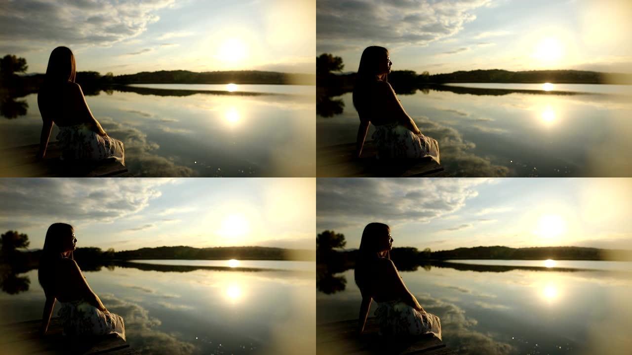 年轻女子在湖码头放松身心，戴着墨镜观看日落。美丽的秋天