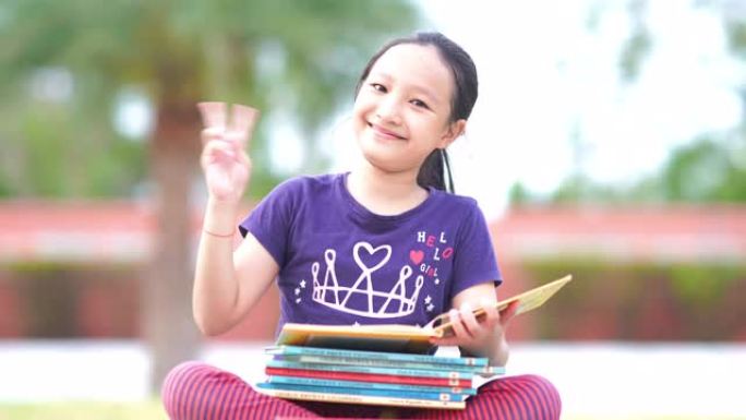 亚洲女孩在花园里读书，成功，胜利标志