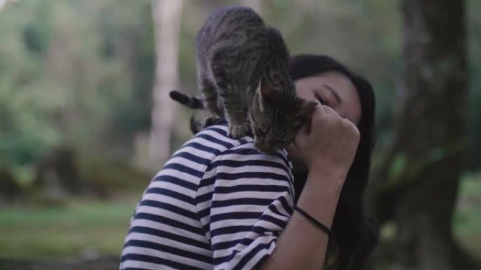 亚洲女孩坐在森林里，可爱的猫站在她的肩膀上。