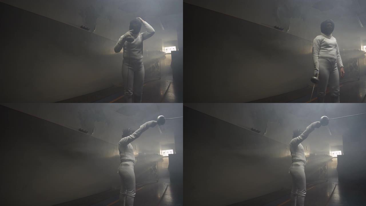 一名女子击剑手在黑暗多雾的训练馆里戴上击剑面具