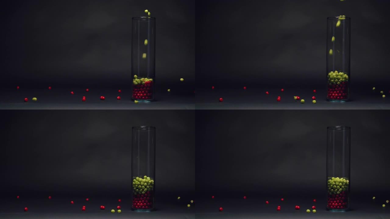绿色糖果落在慢动作的玻璃花瓶中的红色糖果上，黑色黑板纹理背景上的复制空间