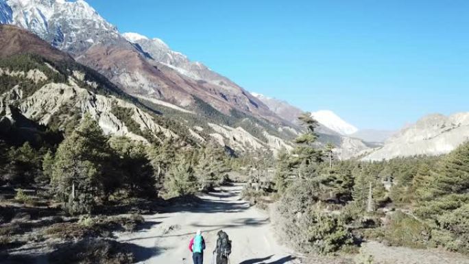 一对夫妇在尼泊尔喜马拉雅山马南山谷的森林中漫步。后面的安纳普尔纳链尖锐而贫瘠的山峰。安纳普尔纳巡回赛