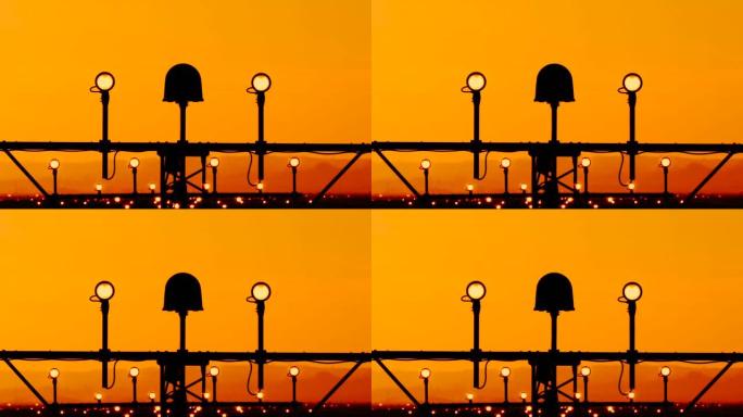 机场跑道边缘灯指示飞机飞行员的着陆路径。灯架着四个侧面的圆形灯和中间的单个大频闪。橙色日落背景下的天