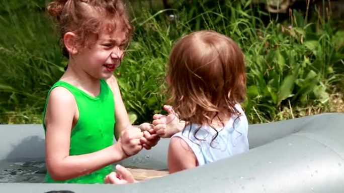 两个小女孩在后院的e充气游泳池内争夺橡皮筋