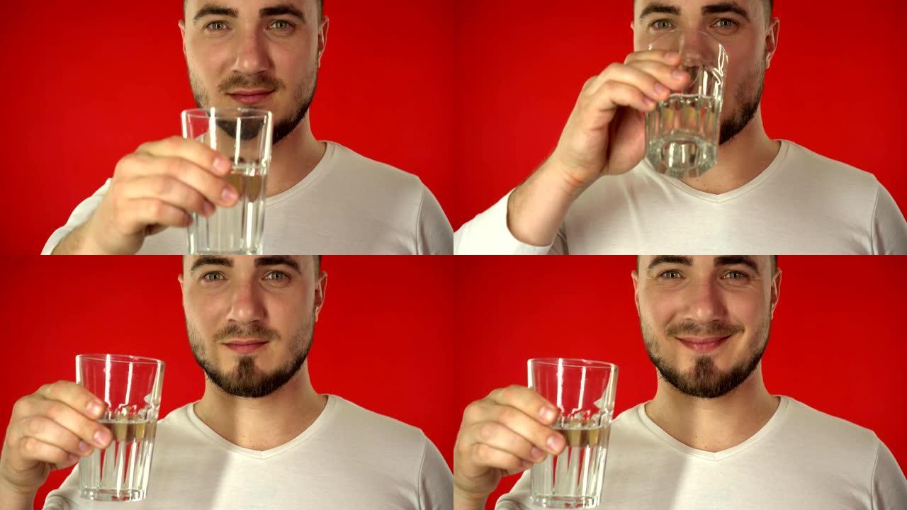 穿着白色t恤的有魅力的男人从红色背景的玻璃杯中喝水。健康的生活方式理念。白人男性拿着一杯水喝在红色背