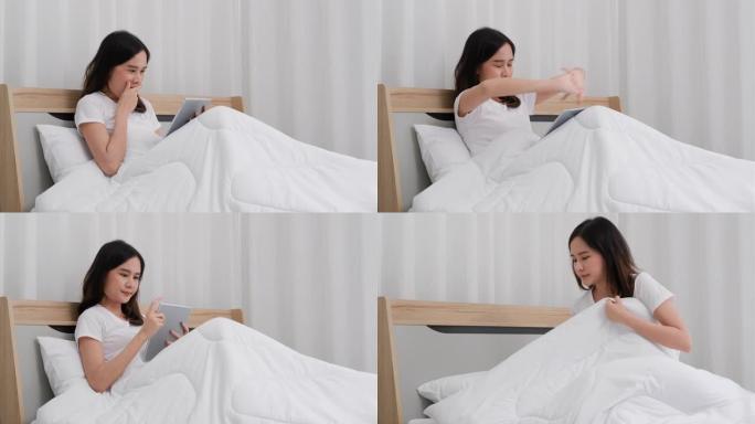美丽的亚洲女人在床上使用平板电脑，打哈欠看起来很困，然后躺在白色床上