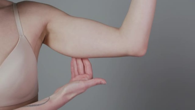 减肥概念。胖乎乎的女人捏上臂脂肪孤立在灰色背景上。高加索女性手部检查松弛皮肤的特写。身体控制，节食的