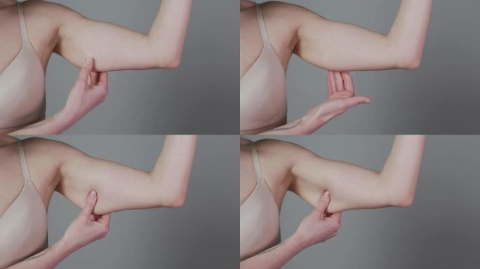 减肥概念。胖乎乎的女人捏上臂脂肪孤立在灰色背景上。高加索女性手部检查松弛皮肤的特写。身体控制，节食的