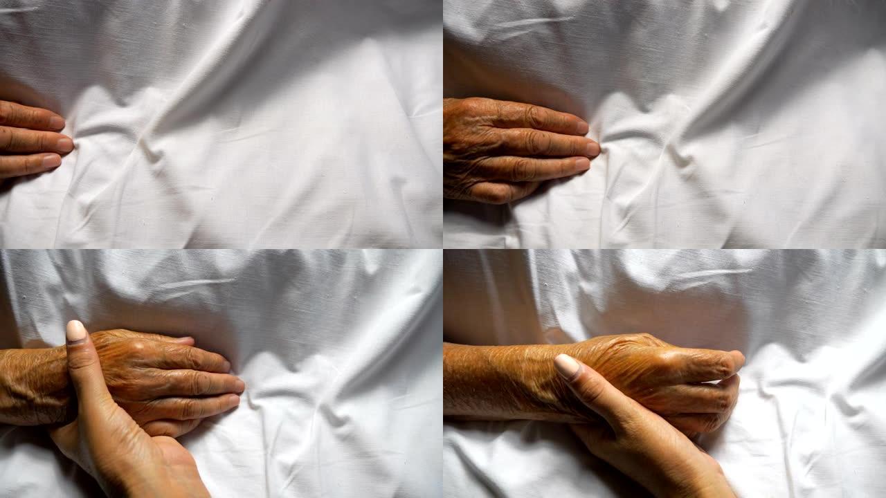 女人握住并轻轻地抚摸母亲的手，表现出关怀或爱心。女儿安慰躺在床上的年迈妈妈皱巴巴的手掌。支持她的老父