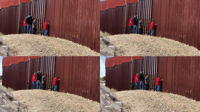 一组四名墨西哥人透过边境围栏望向美国一侧的国际边境墙